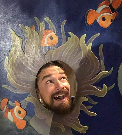 Travis Knorr with his face sticking through a painted cutout of anemone surrounded by clownfish